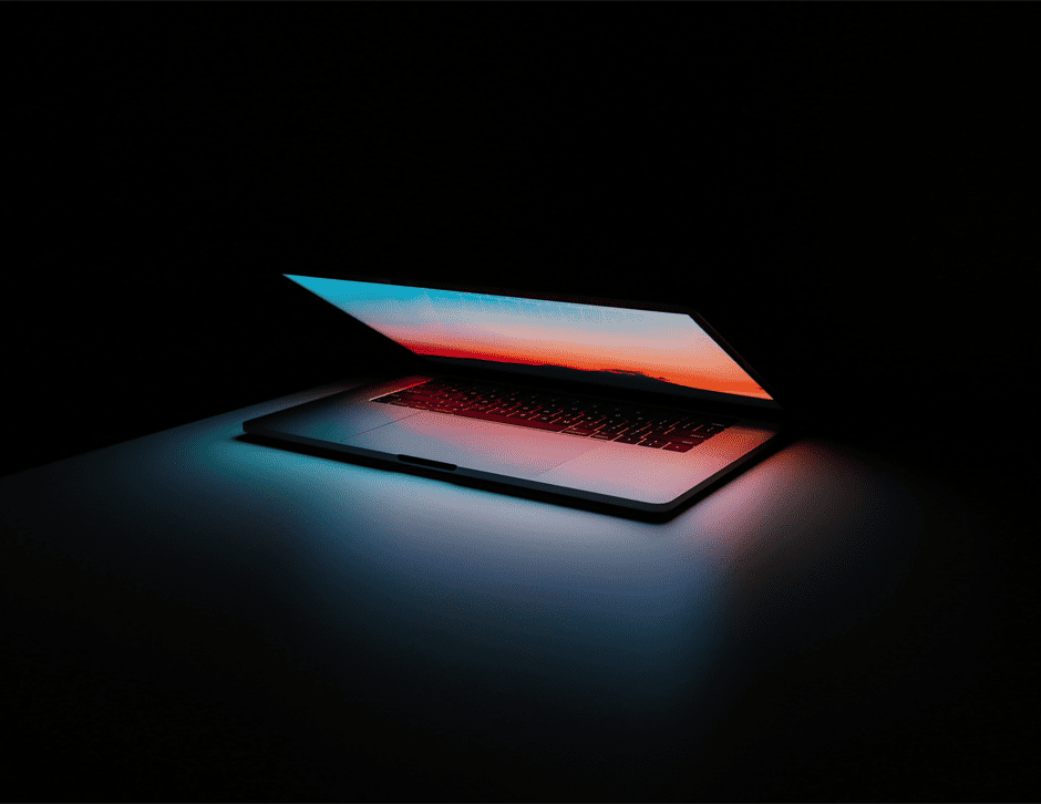 Laptop entreabierta con fondo de inicio en la pantalla en un entorno oscuro que se ilumina con la luz de la pantalla.