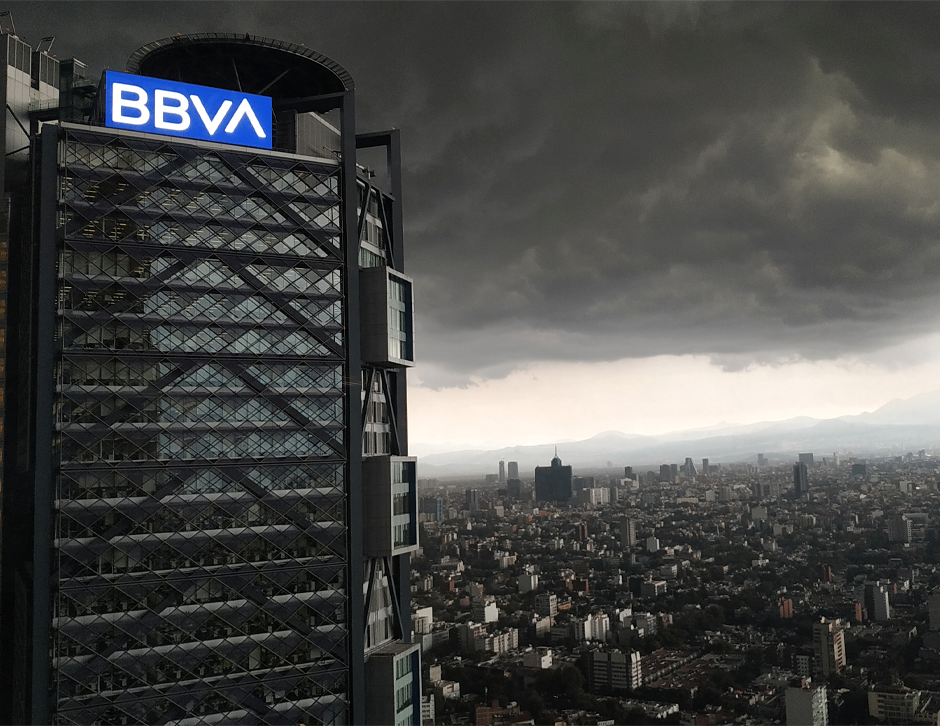 A black and white photo captures the view of the BBVA building on Reforma Street in Mexico City, with other buildings of the city visible in the background.